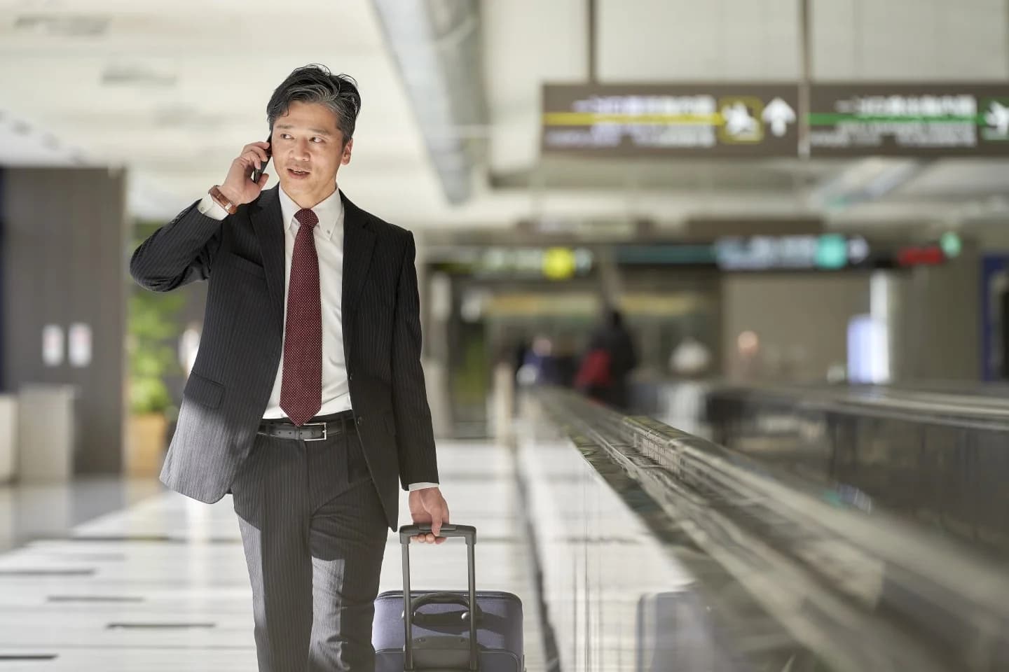空港の外でスーツケースを抱えるスーツを着た男性